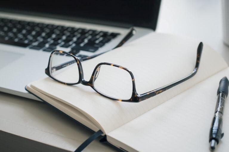 Glasses on top of a notebook next to a laptop